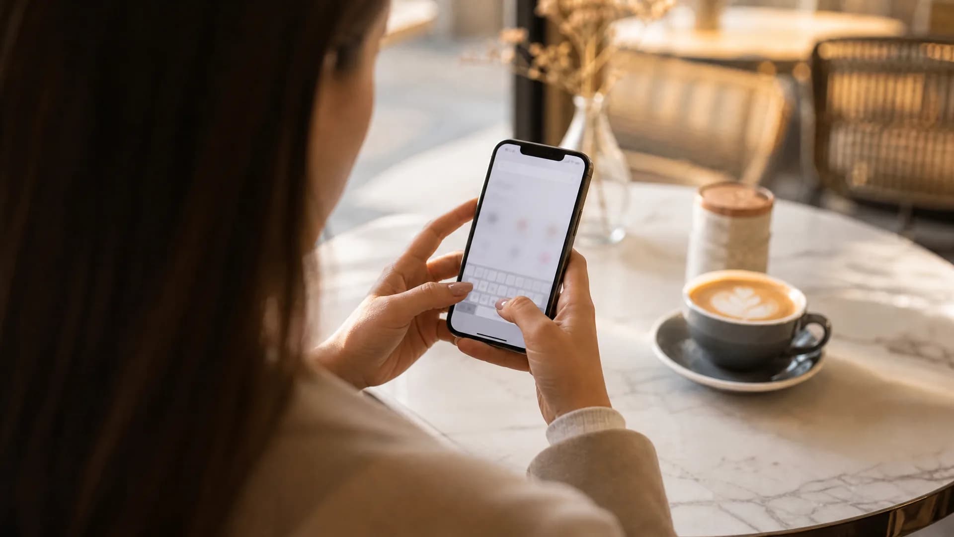 A woman typing into her phone's browser address bar at a sunny café